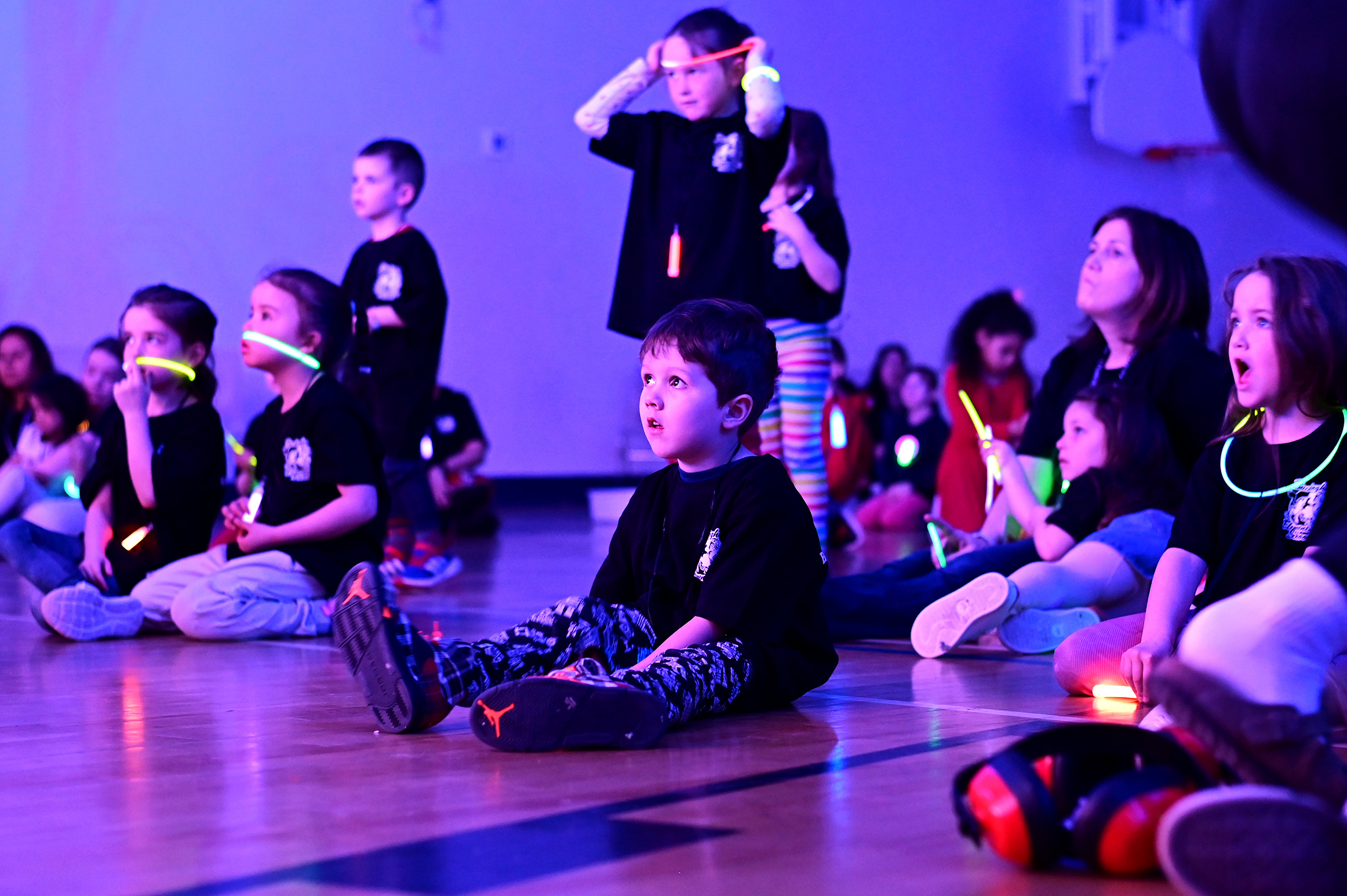 Students watching the concert, all a-glow with glowstick necklaces and bracelets in a black lit gym.