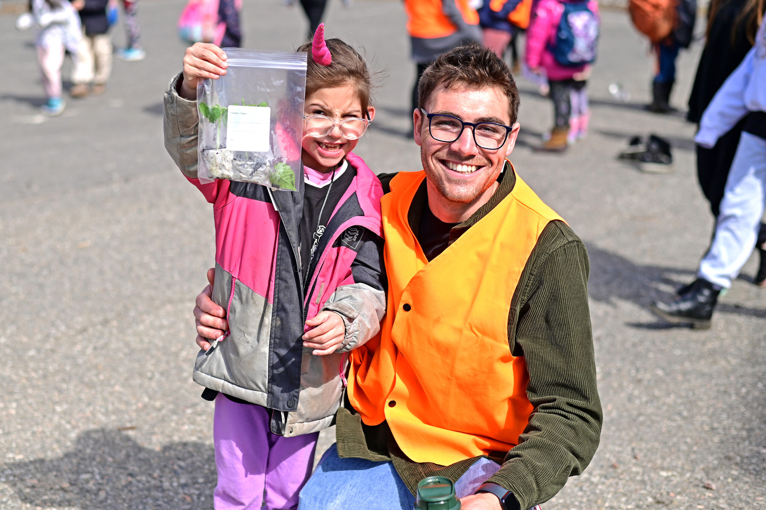 Student and teacher pose together at bus time. Student is proudly holding up the basil she grew in class.