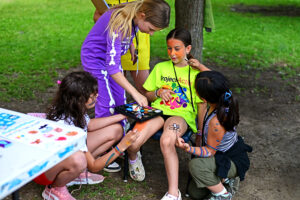 Three students at the face-painting station painting one student all over