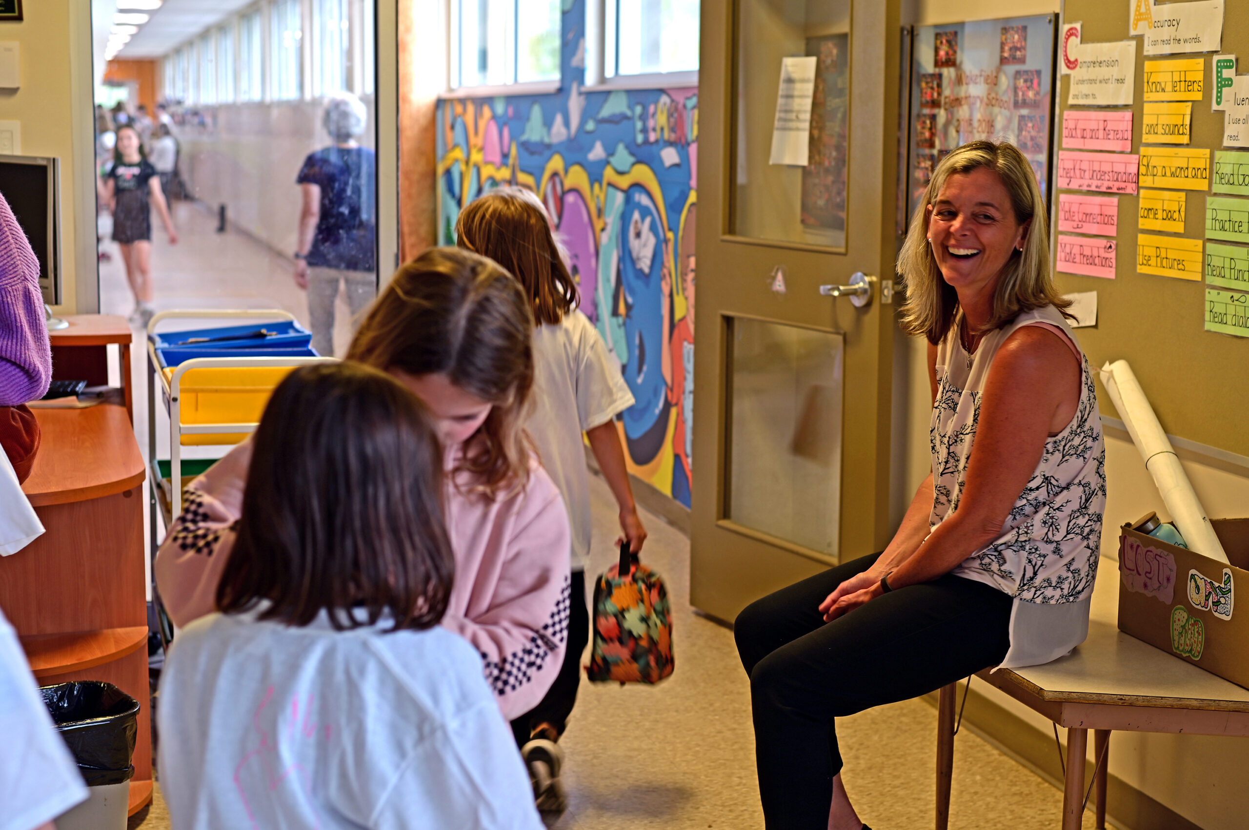 Principal Julie Fram-Greig sits by the library door, saying goodbye to the students as they exit to go back to class
